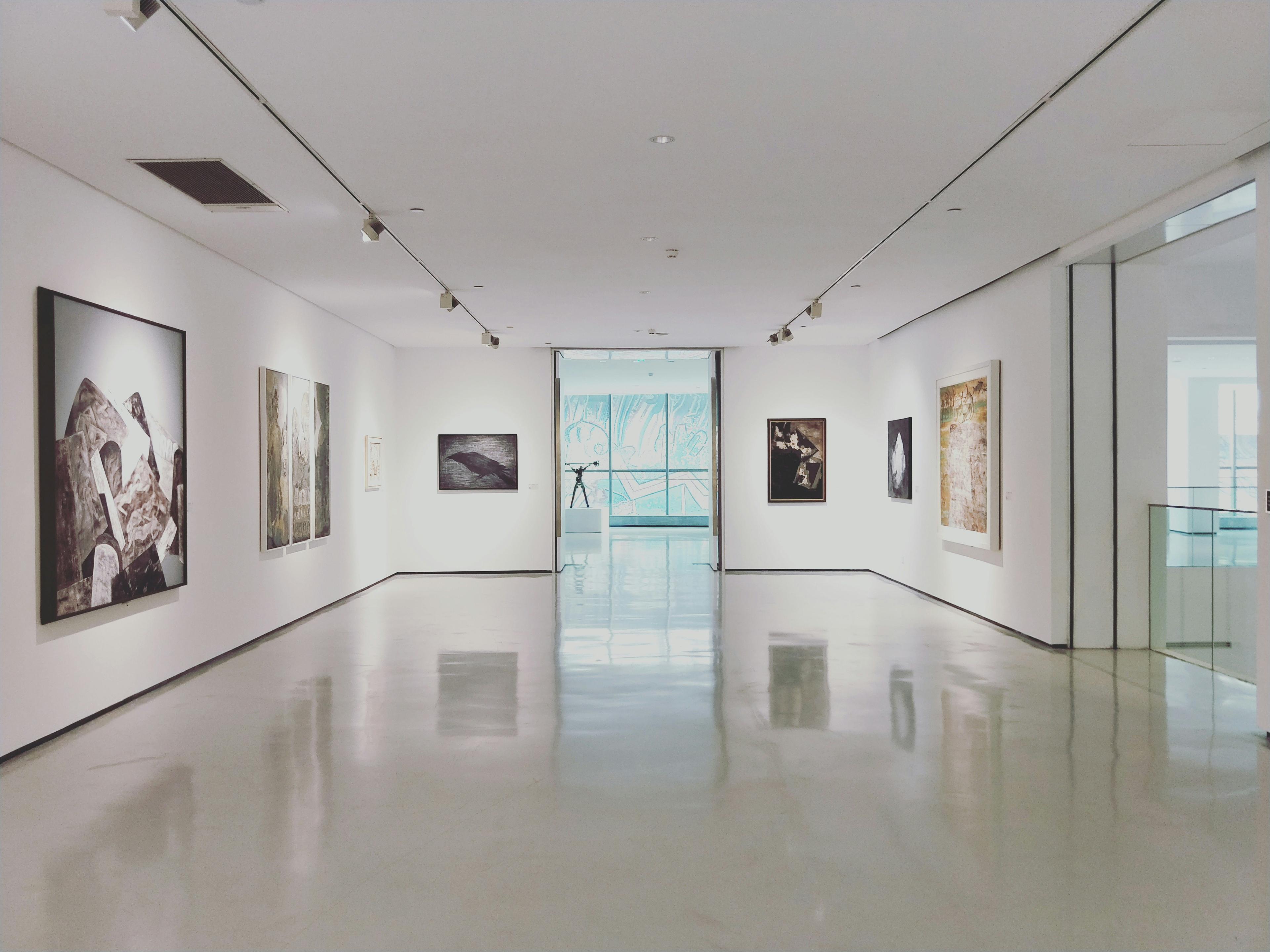 A modern gallery hall with framed paintings on white walls and a polished floor