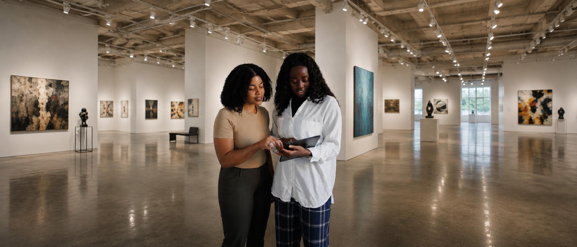 Two colleagues reviewing a collection on a tablet in a contemporary gallery.