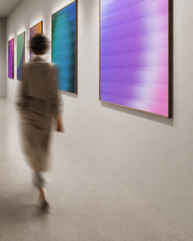 A visitor walking through a gallery past framed abstract paintings